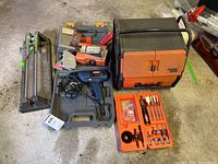 Photo shows multiple Black and Decker plastic hardware cases closed and open, the Ryobi corded drill, assorted drill bits in an orange case, and hardware boxes on concrete floor.