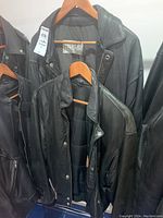 Two black leather jackets hanging on wooden hangers, showing overall front view and condition.