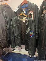 Two black leather jackets hanging on rail: front Avirex bomber and back Shain jacket