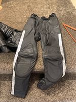Top view of one pair of black leather motorcycle pants showing padded knee areas and reflective stripes on sides