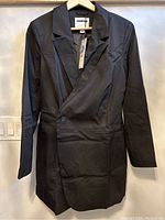 Front view of black blazer dress on hanger, single button closure, tailored fit.
