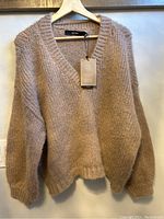 Front view of the brown v-neck chunky knit sweater hanging on a hanger, showing texture and style.