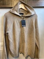 Full view of the wheat colored ribbed knit cardigan hanging on a wooden hanger, showing full front zipper and high neck collar.