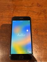 Front view of the iPhone SE 2020 powered on showing welcome screen 'hello'. Minor wear around edges visible.