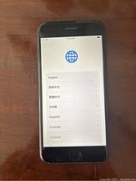 Front view of iPhone SE 2020 showing language setup screen with options like English, Chinese, Spanish, French, German.