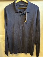 Blue long-sleeve polo shirt hanging on a wooden hanger showing full front view with collar and two buttons on placket visible. Shirt appears in like new condition without visible defects or stains.