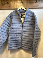 Front view of blue puffer jacket hung on wooden hanger showing full front and sleeves