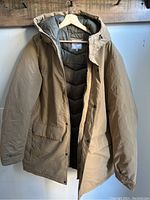 Front view of the khaki jacket hanging showing hood, sleeves and overall condition with zipper partially open.