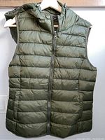 Front view of green puffy vest hanging on hanger showing zipper front and quilted pattern.
