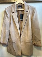 Light brown women's loose blazer on hanger, showing front with two flap pockets and visible creases.