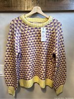 Front view of medium size yellow and purple patterned pullover sweater hanging on a wooden hanger.