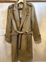 Front view of long beige wool coat with belt and button details on cuffs and shoulders