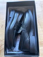 Side view of black leather loafers in original box showing textured leather and low heel.