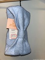 Front view of the blue knit head band showing the knot detail and attached tags.