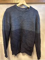 Full view of blue knit sweater with a gradient from lighter blue on top to dark blue at bottom, hanging on a wooden hanger showing entire garment