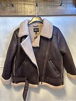 Front view of brown faux leather aviator jacket with cream sherpa collar, zipped front, zippered pockets, and belted hem.