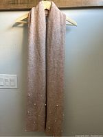 Front view of light pink ribbed knit scarf with pearls on edges, hung on hanger.