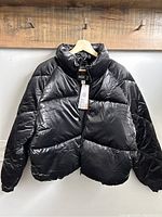 Front view of a black women's puffer jacket hung on a wooden hanger.