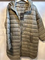 Full front view of the women's quilted coat revealing horizontal quilting, zipper, hood, and olive green color.
