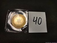 Photo of the commemorative medal/token inside a clear protective sleeve beside a paper with number 40 for lot identification.