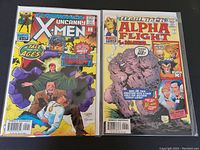 Photo shows front covers of Uncanny X-Men #-1 and Alpha Flight #-1 comics in protective sleeves on a dark surface.
