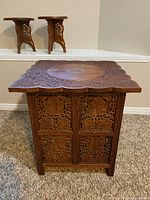 Front view of the carved teak side table showing side panels and detailed floral carving