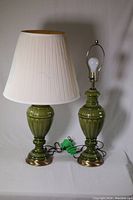 Pair of green ceramic table lamps shown side by side with one lamp having a white pleated lamp shade.