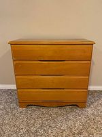 Front-facing view of the 4-drawer wood dresser showing natural wood finish, straight lines, no drawer handles, and carved base.