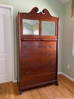 Full front view of the antique wooden armoire showing multiple drawers and two bevelled mirrored doors at the top with decorative carved wood detail.