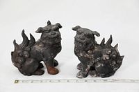 Pair of antique cast iron Chinese Foo dog statues placed side by side on a white surface with a measuring tape showing approximately 7 inches length.
