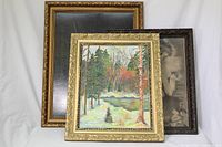 Framed landscape painting with trees and a river, colorful autumnal scene, gold ornate frame, in front of two other frames with black and white prints.