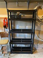 Full view of black plastic shelving unit with five shelves and open-grid surfaces