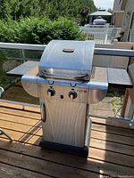Front view of Char-Broil Tru-Infrared 2-burner BBQ grill with closed lid, control panel, and side shelves. Shows general condition including signs of rust and wear. Attached propane tank visible.