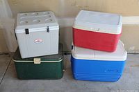 Four coolers stacked: vintage green metal Coleman cooler, gray/white electric 9V cooler with cup holders, red Rubbermaid cooler, blue Igloo cooler.