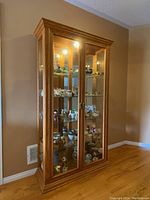 Full view of wood display cabinet with glass shelves filled with small collectible items, light on inside.