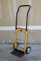 Yellow dolly with black handles standing upright on a concrete floor against a light wall.