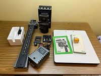 Durst AC 650 film enlarger and accessories arranged on table including power supply, film holders, red light filter, spare bulb, and manuals.