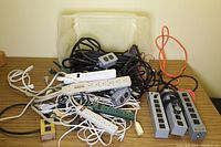 Overview photo showing variety of power bars, power strips and extension cords tangled inside plastic container.