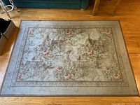Top view of the rectangular floor rug showing floral and ornate design, colors beige, green, pink, on a wooden floor.