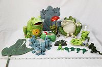 Wide shot showing all frog-themed items grouped together on a white background, including thermometer, pot holders, soap dish, soap pump, key hook, and assorted frog figurines.