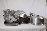 Overview of assorted baking pans piled together showing loaf pans, cake pans, springform pans and cake plate with cover.