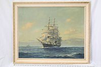 Framed painting or print of a sailing ship on the ocean, showing the ship with full sails in the foreground and another ship in the background, frame is cream-colored with a decorative border.