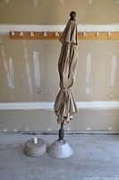 Umbrella standing folded with two bases placed next to it inside a garage.