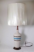 Front view of tall retro lamp with beige/cream ceramic base decorated with brown and blue stripes, wood accents, and white lampshade.