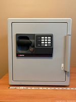 Front view of closed safe on table showing electronic keypad, handle, Sentry logo and measuring tape