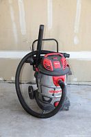 Shop-Vac wet/dry vacuum cleaner with hose, attachment tools, and wheels visible.