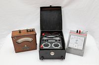 All three meters shown together: wooden Weston ammeter on left, open black Avometer 8 in middle, gray Armco galvanometer on right