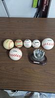 3 banks, 7 balls and a trophy arranged on a wooden surface showing different baseball and softball balls, coin banks, and a trophy.