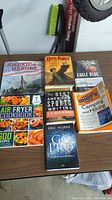 Wide view of seven assorted books on a table including history, fiction, sports writing, and cookbooks.
