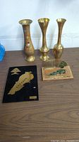 Photo showing three brass vases and two Lebanese-themed decorative plaques on a wooden table.